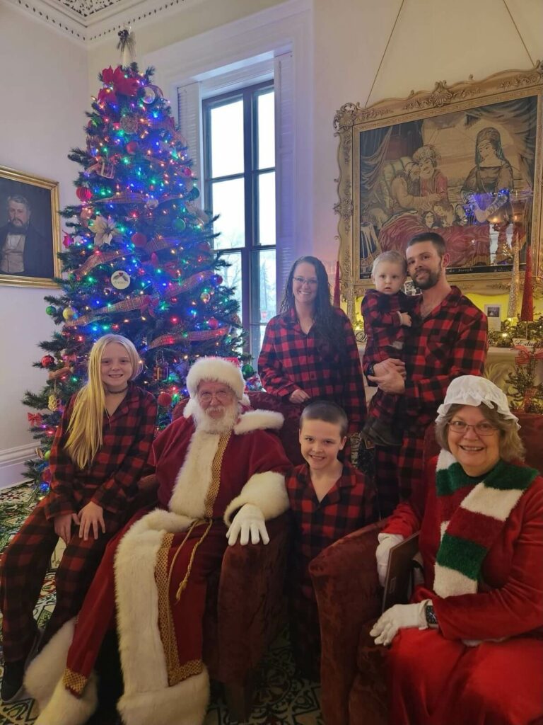 A family poses for a photo with Santa Claus in front of a Christmas tree